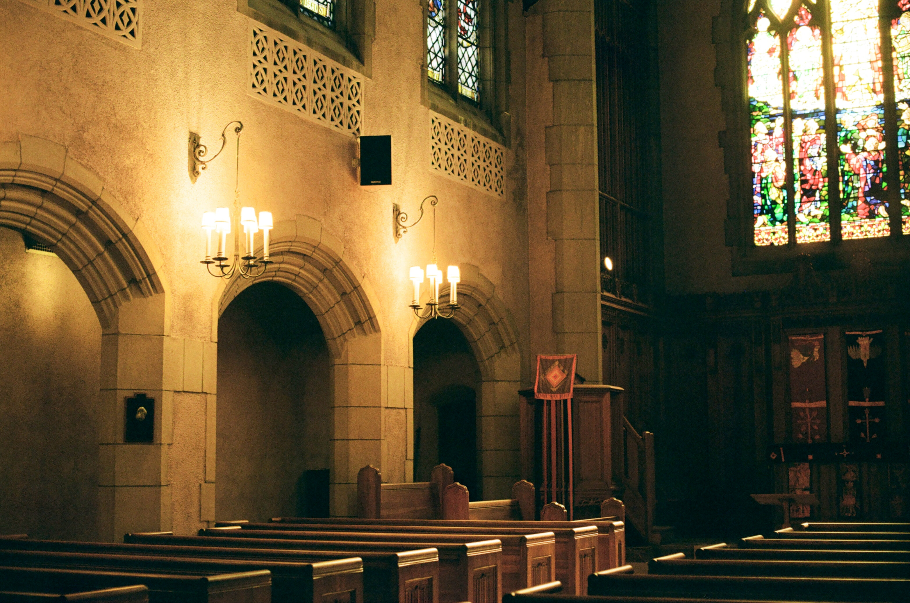 Wood-paneled chapel lit by sunlight entering through a large arched stained-glass window
