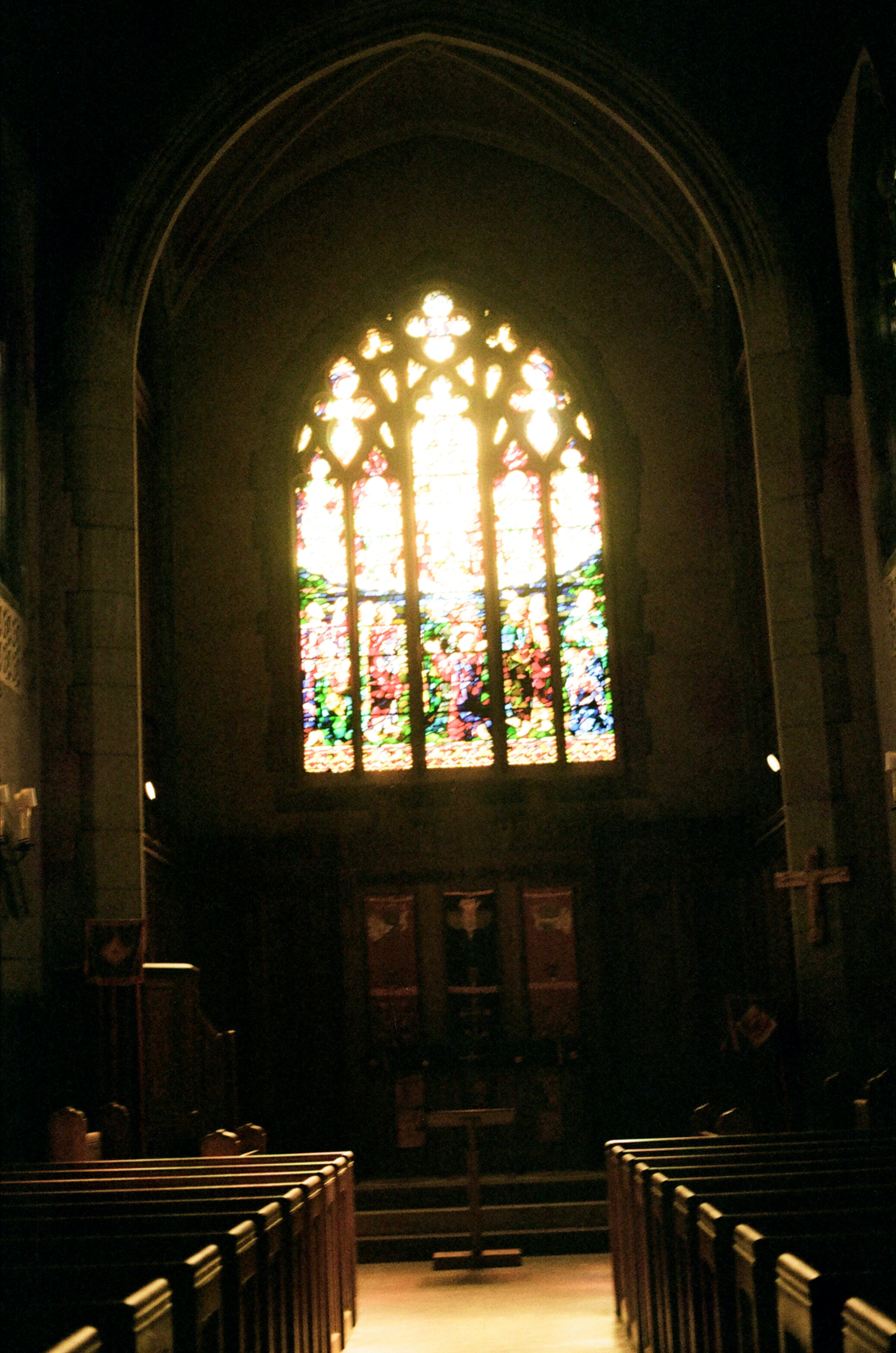 Wood-paneled chapel lit by sunlight entering through a large arched stained-glass window
