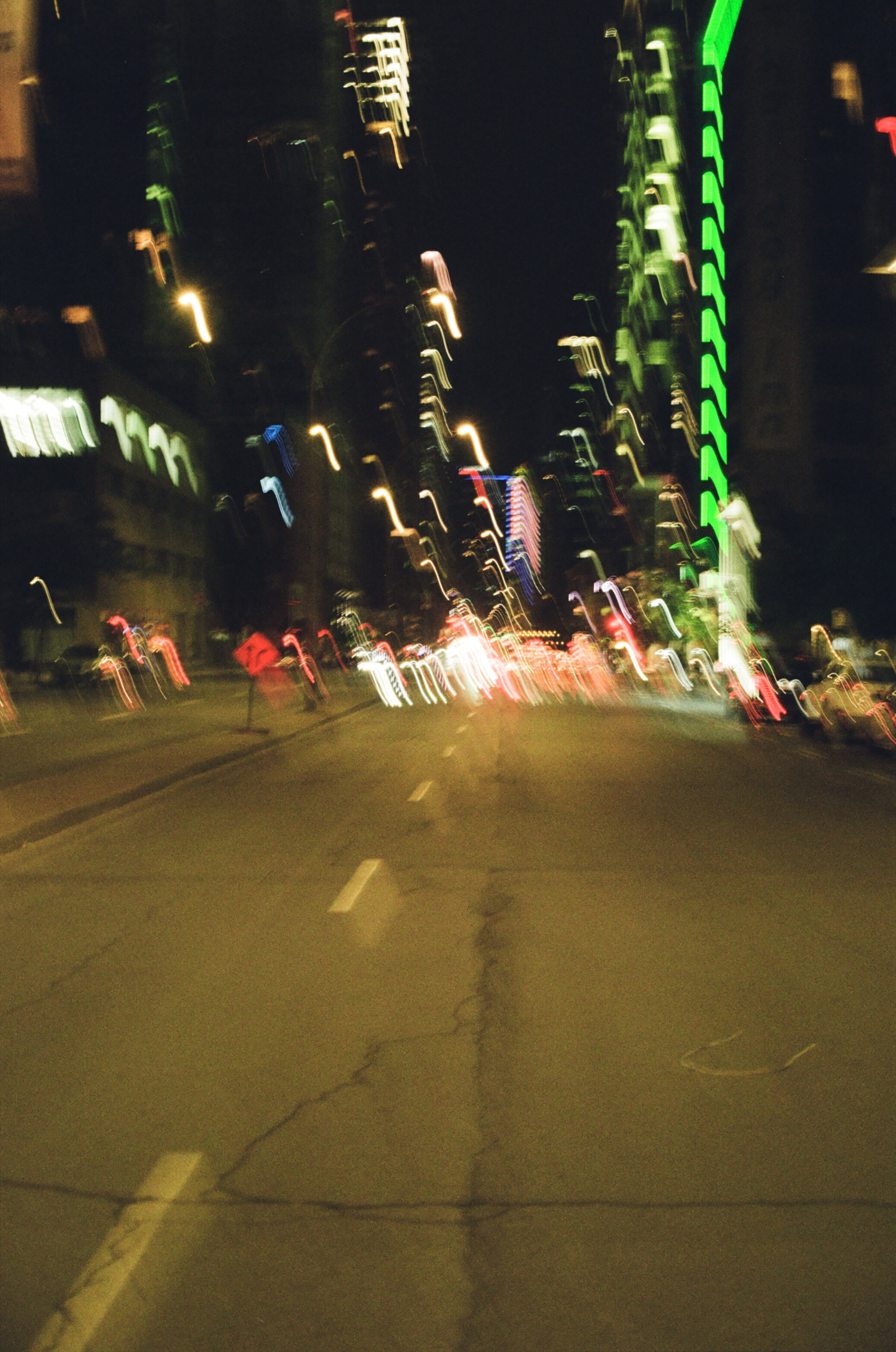 A city street surrounded by tall buildings at night, with severe motion blur from an unsteady camera