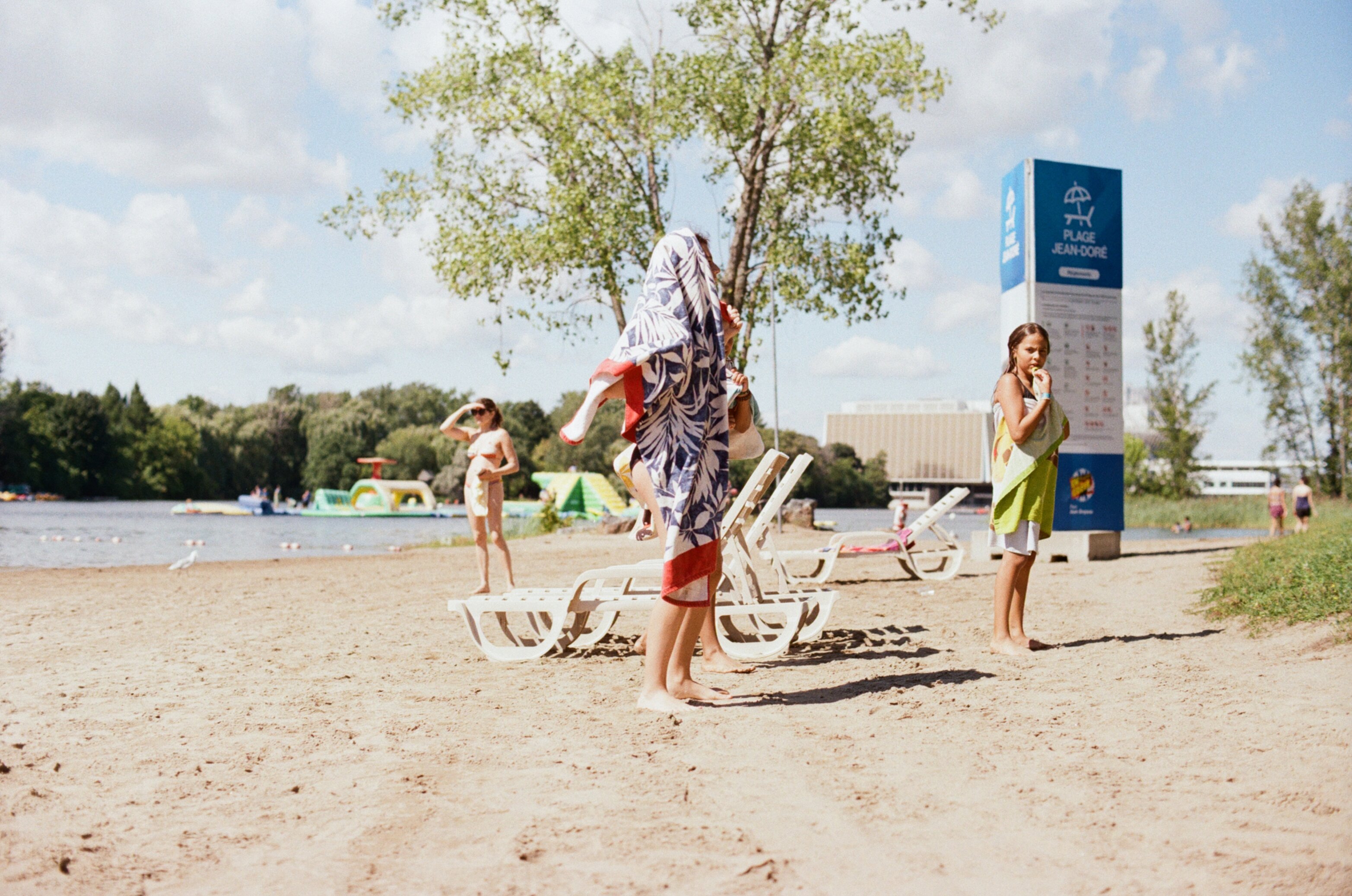 A boy stands on the sandy beach with his head covered by a towel