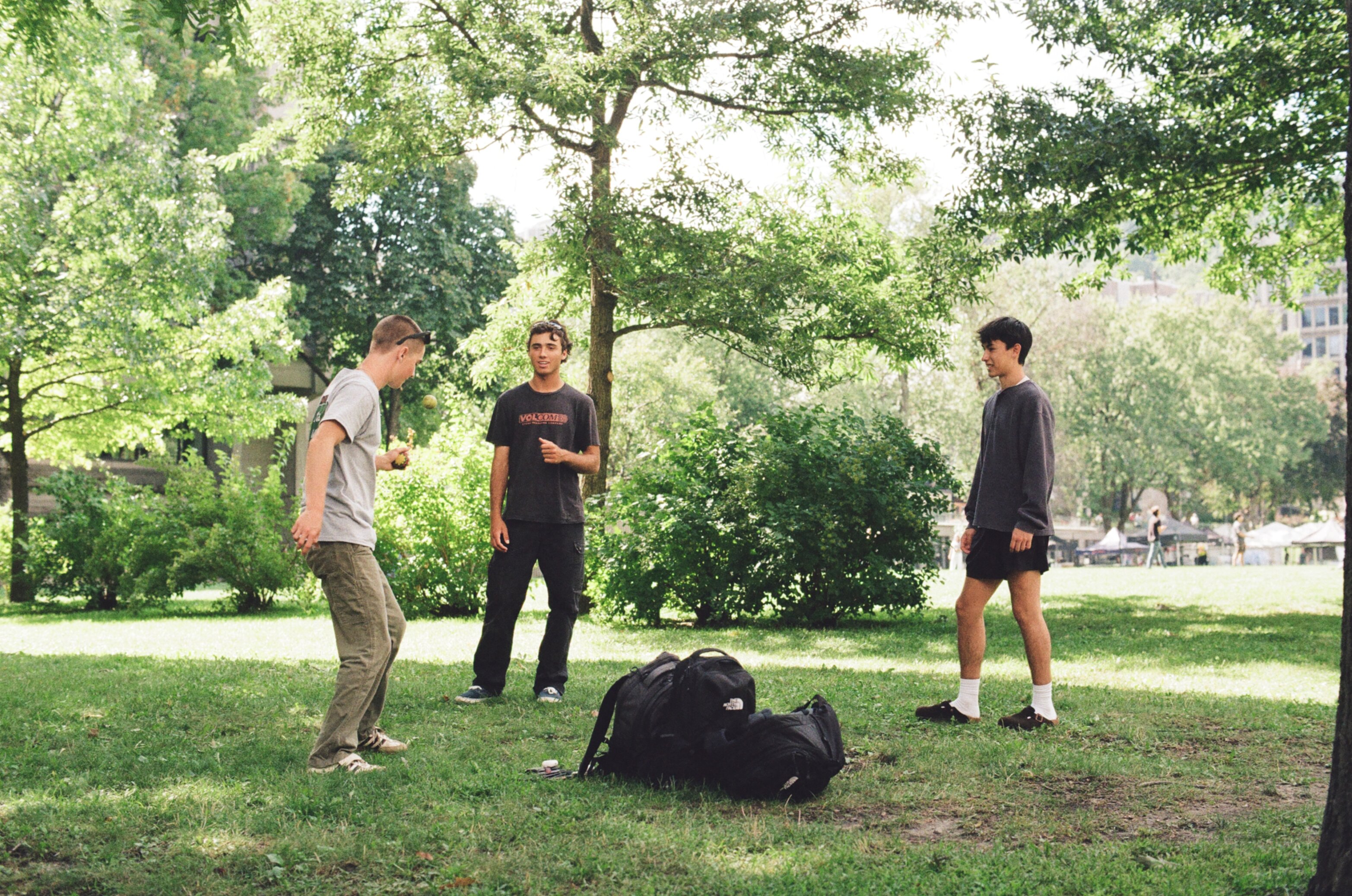 Three men on the grass in the shade passing around a small ball