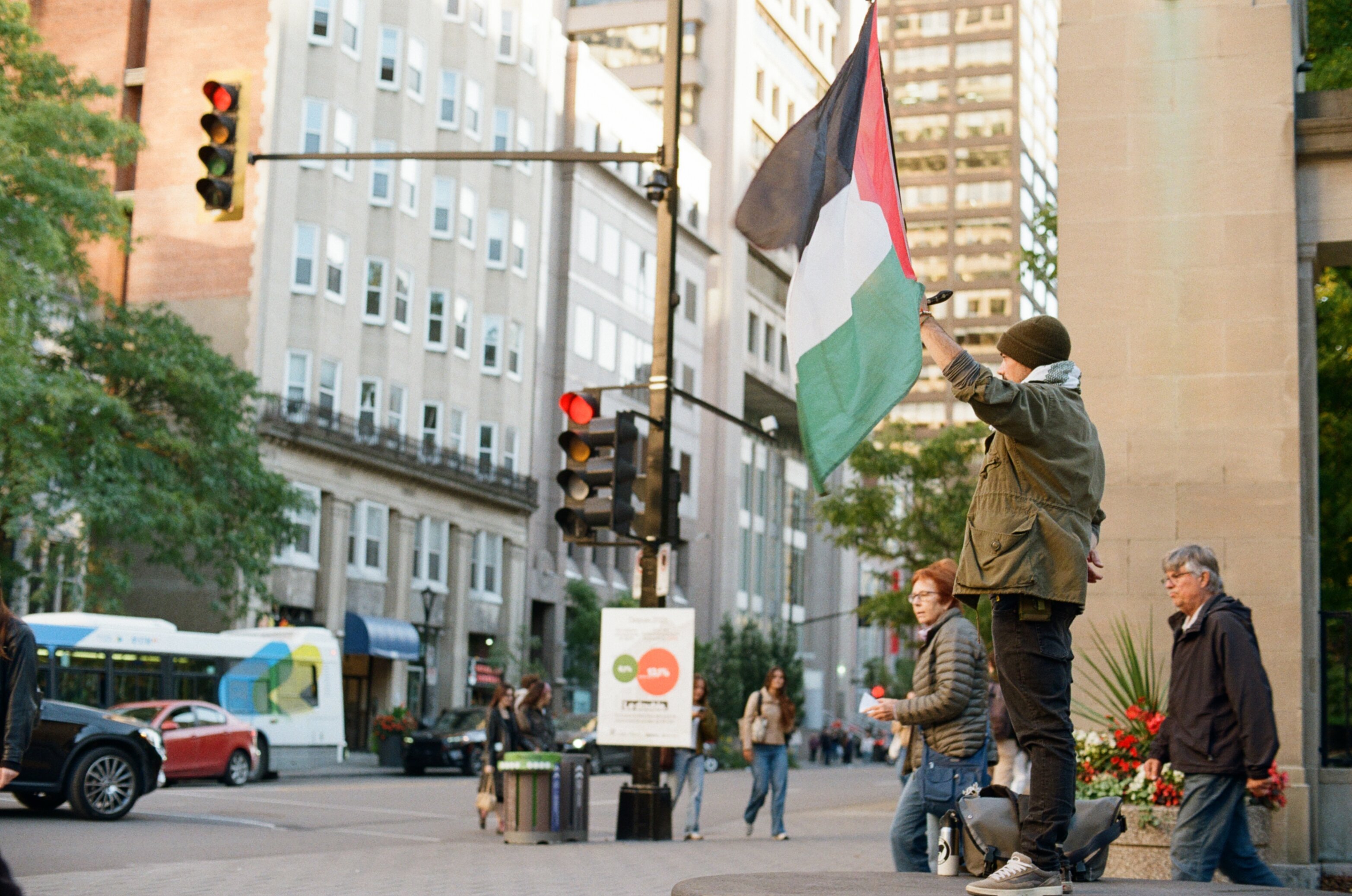 Man standing on a stone bench holding up a Palestinian flag in front of a stone gate
