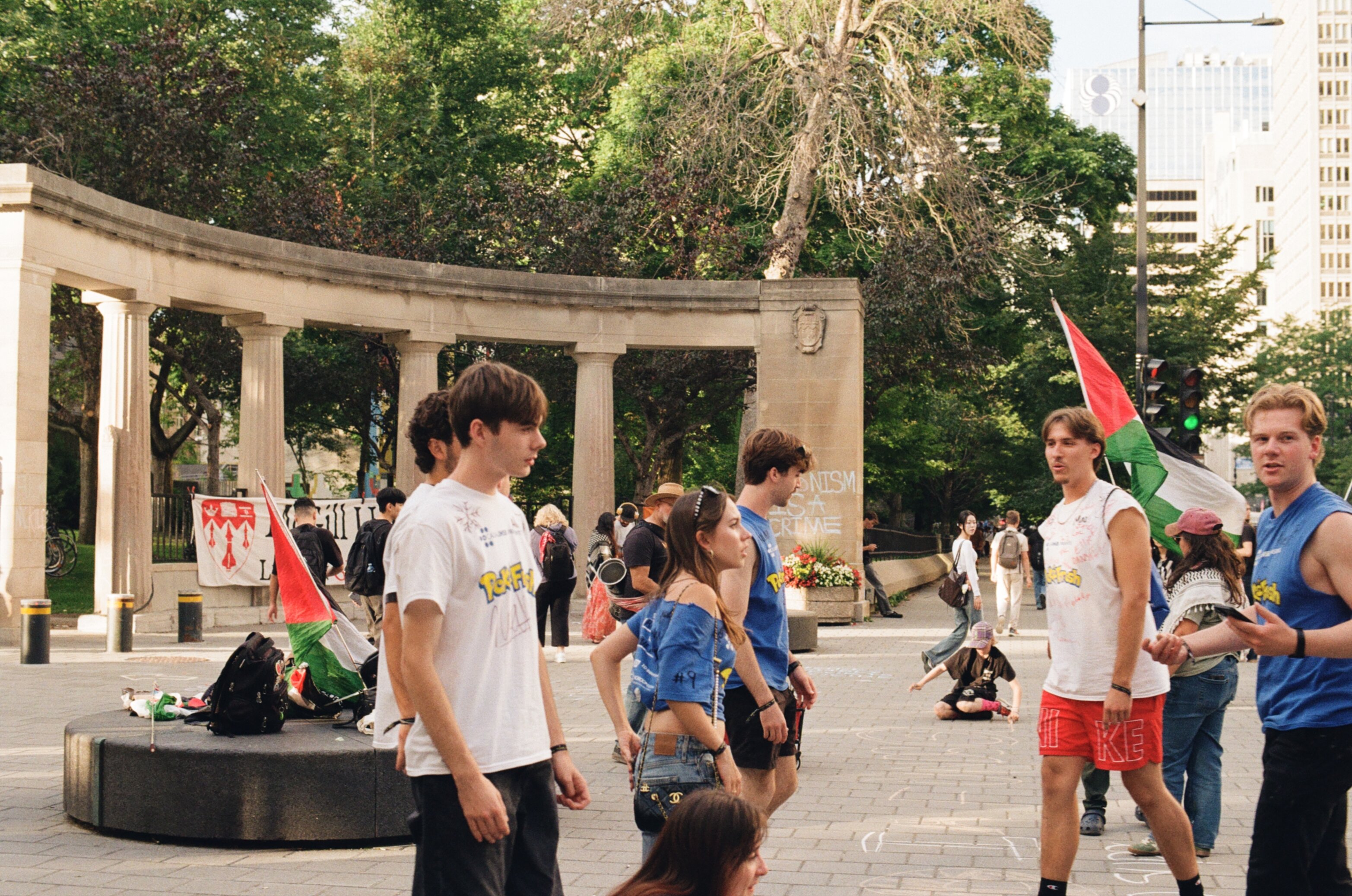 Students pass by a group of demonstrators with a sign in the background that says 'McGill University Leads in GENOCIDE Funding'