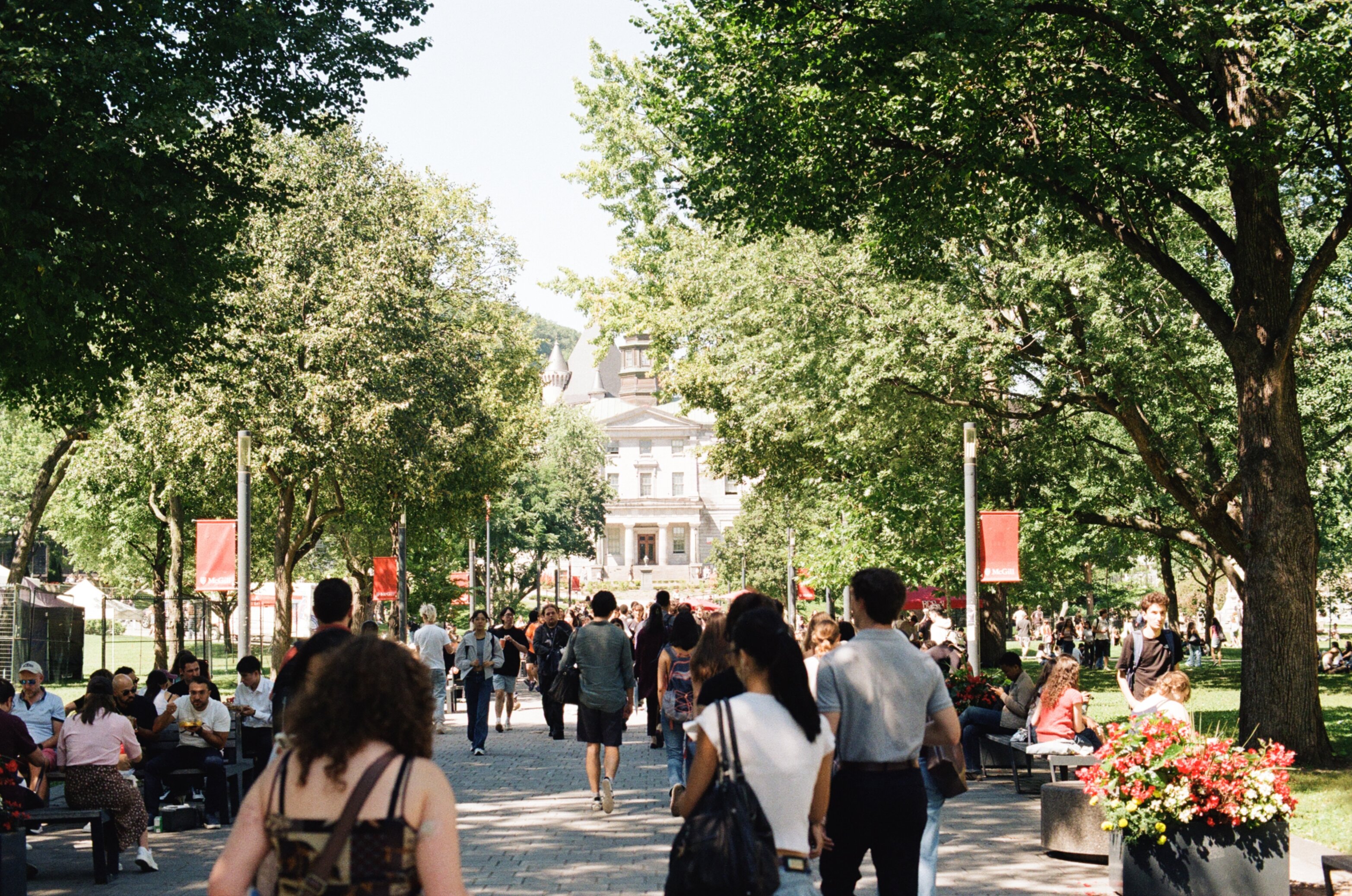 Crowd of students walking along a path towards a stone building with pillars and a cupola