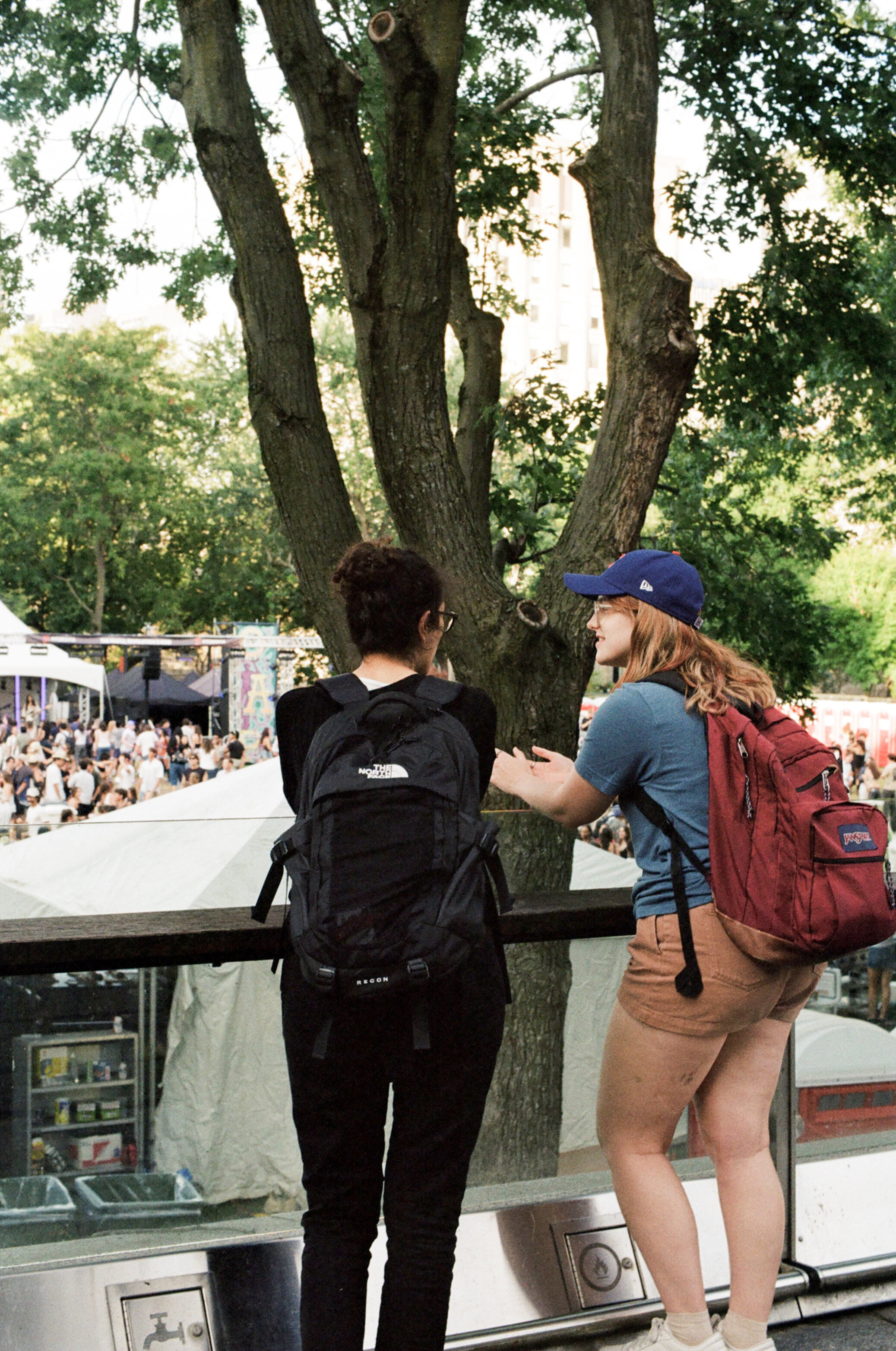 Two women on a balcony overlooking a crowd at an outdoor concert