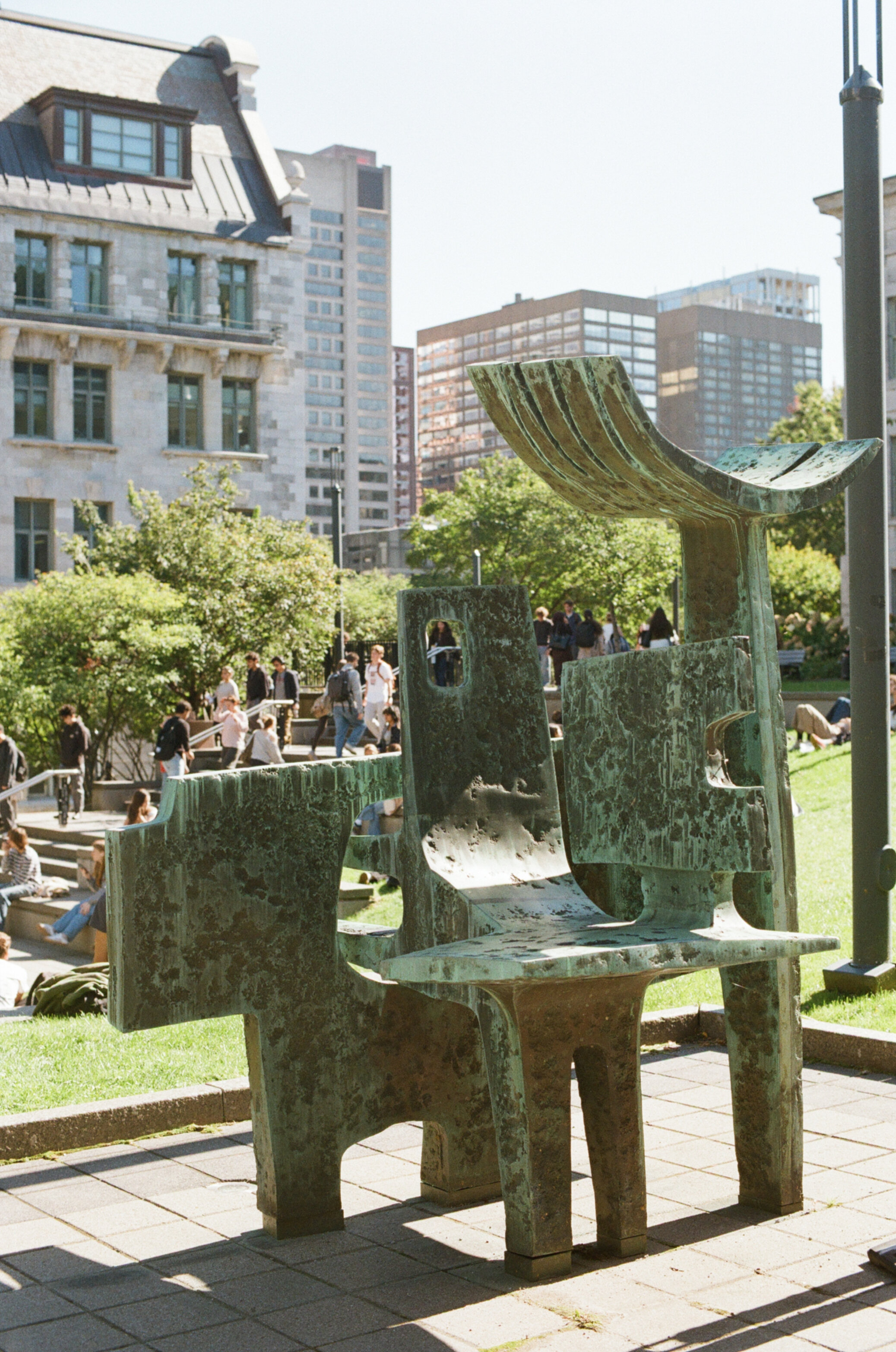 Weathered green metal sculpture with students sitting on stepped grass in the background