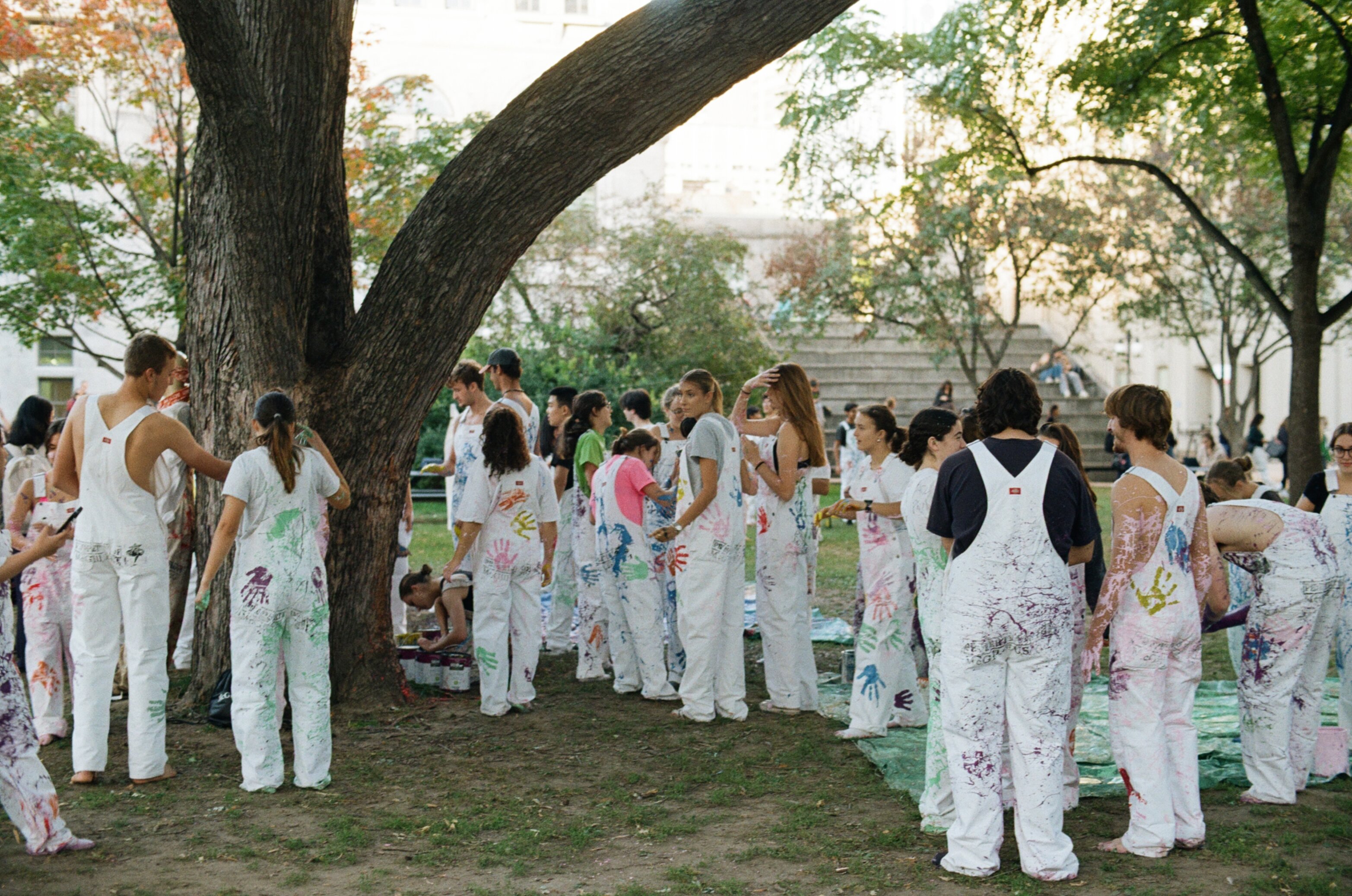 Group of students standing in a grass field all wearing white overalls covered in colourful paint splashes