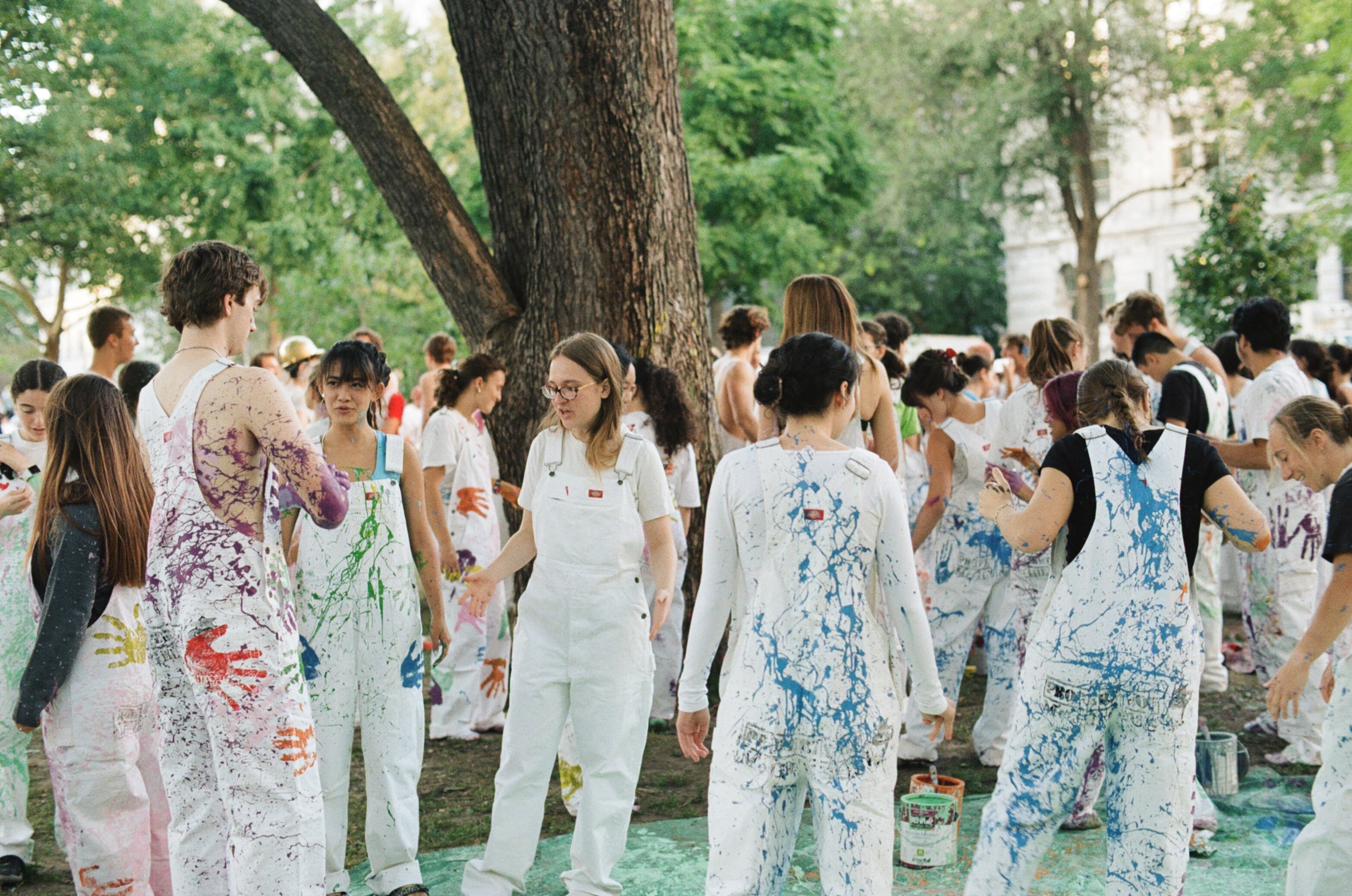 Group of students standing in a grass field all wearing white overalls covered in colourful paint splashes