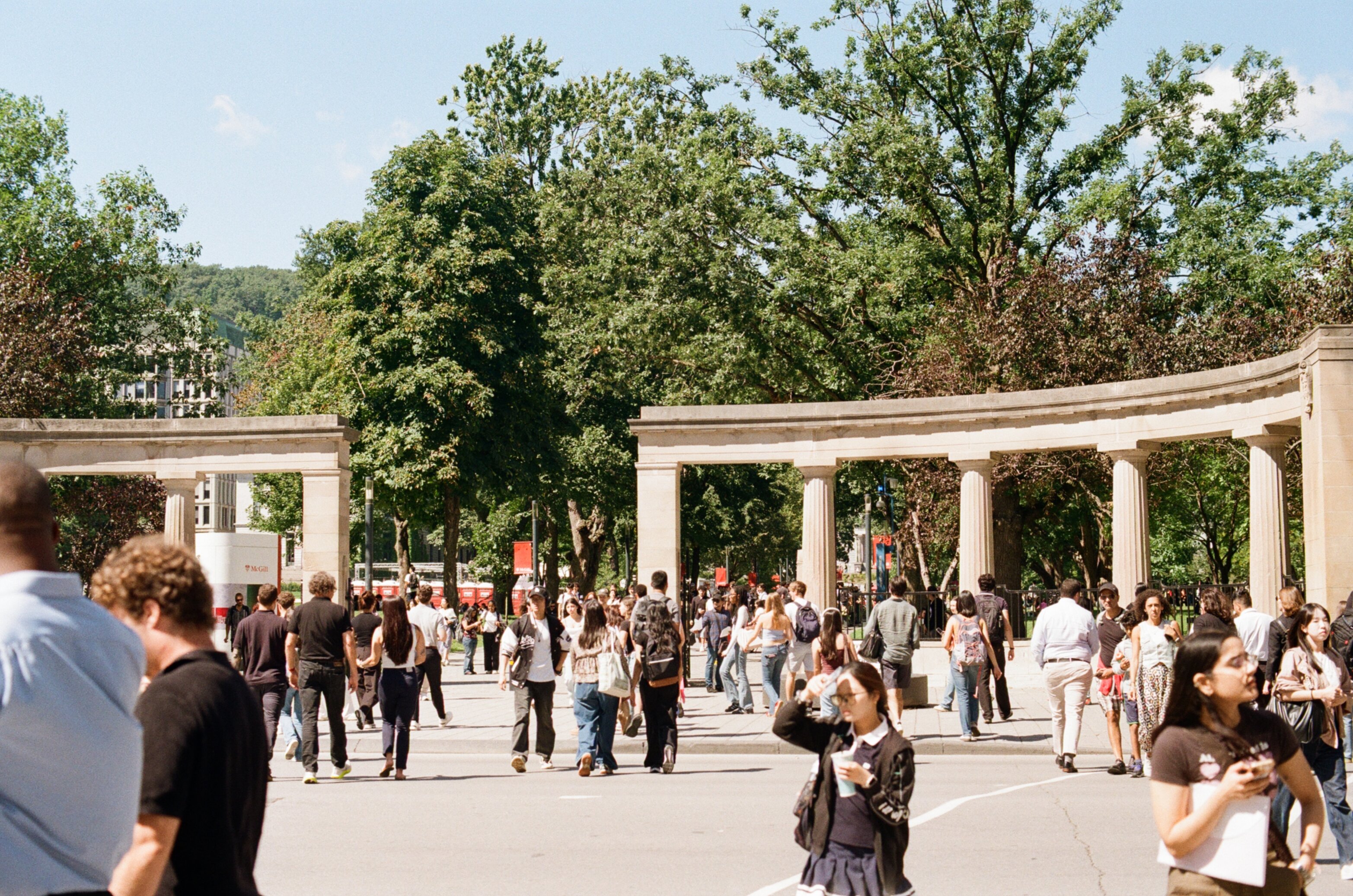 Crowd of students crossing the street with stone pillars in the background