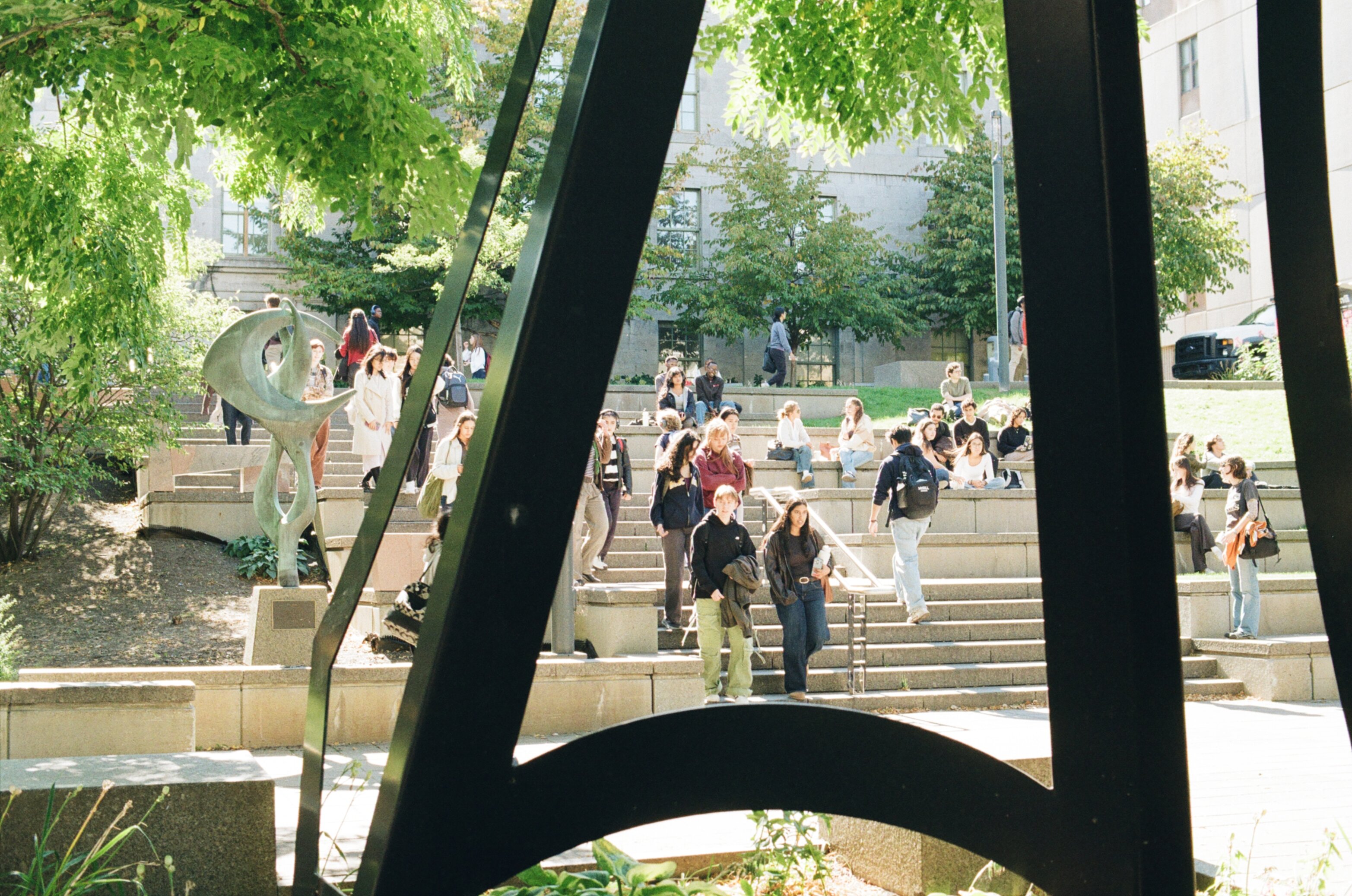 Students walking down stone stairs outside viewed through a black sheet metal sculpture