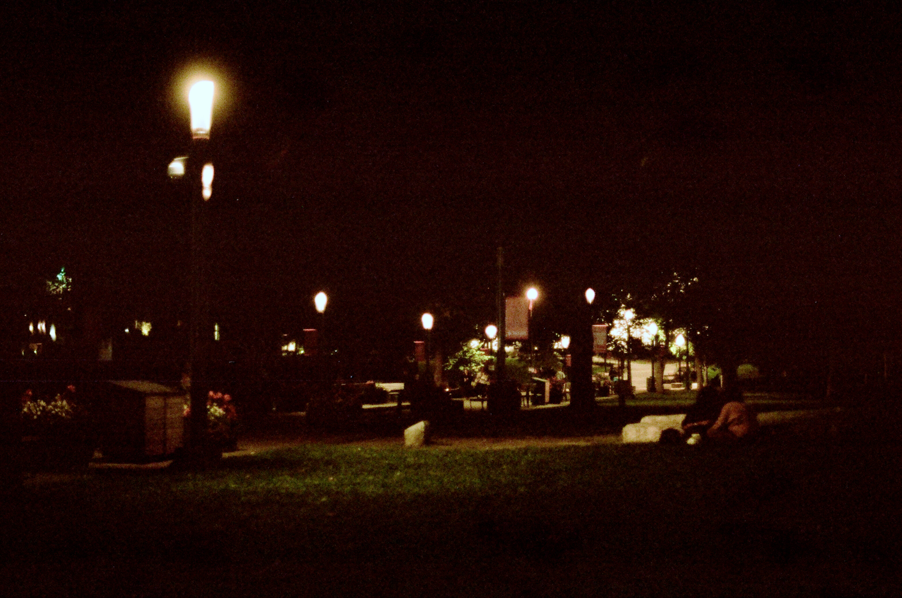 Two female students sit on a grass field lit by street lamps at night