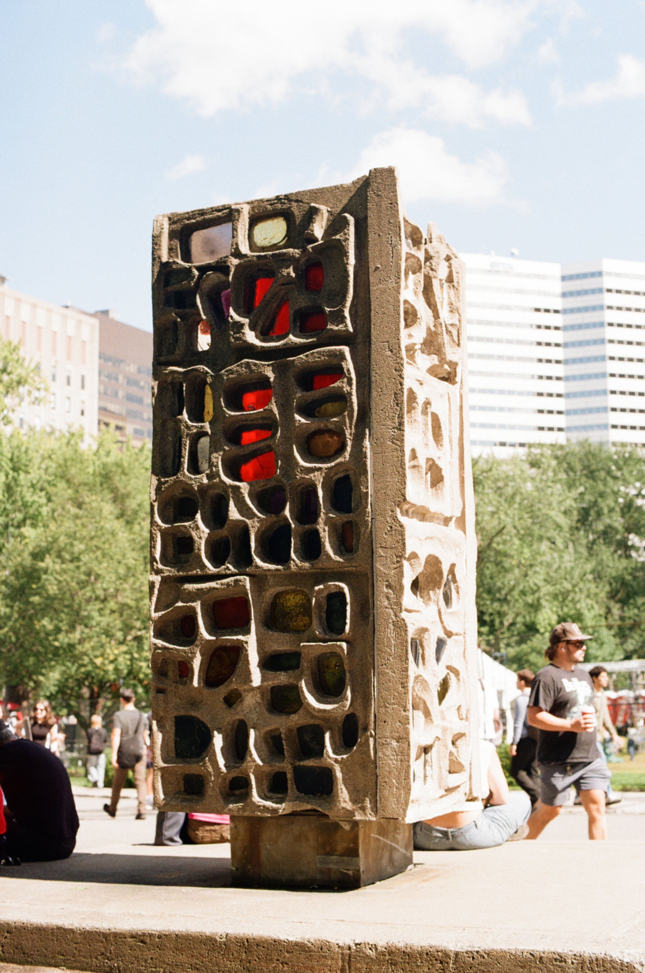 Students sitting around a large cuboidal concrete sculpture with many holes filled with stained glass