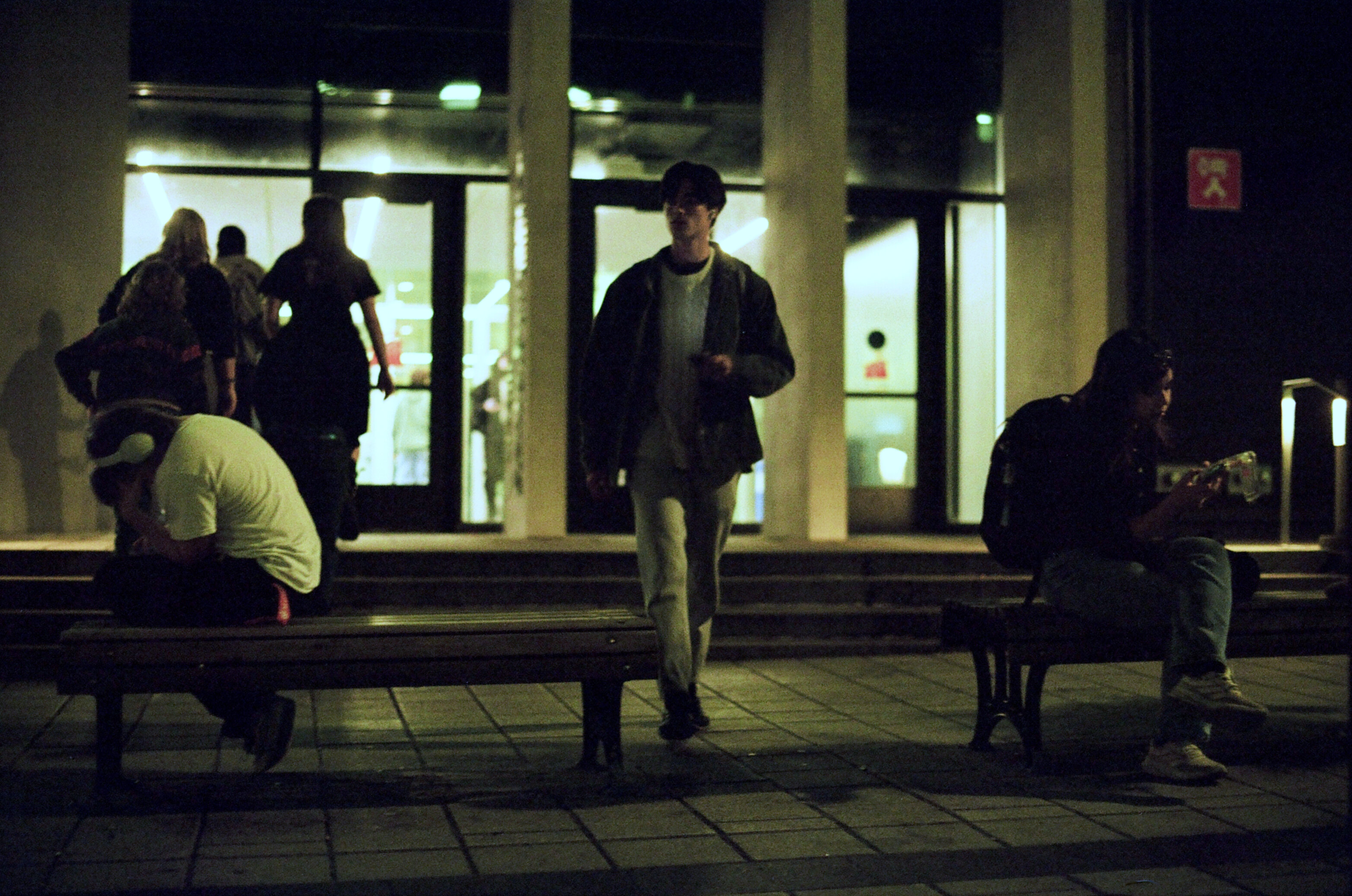 Students exit a university building into a dimly-lit street at night