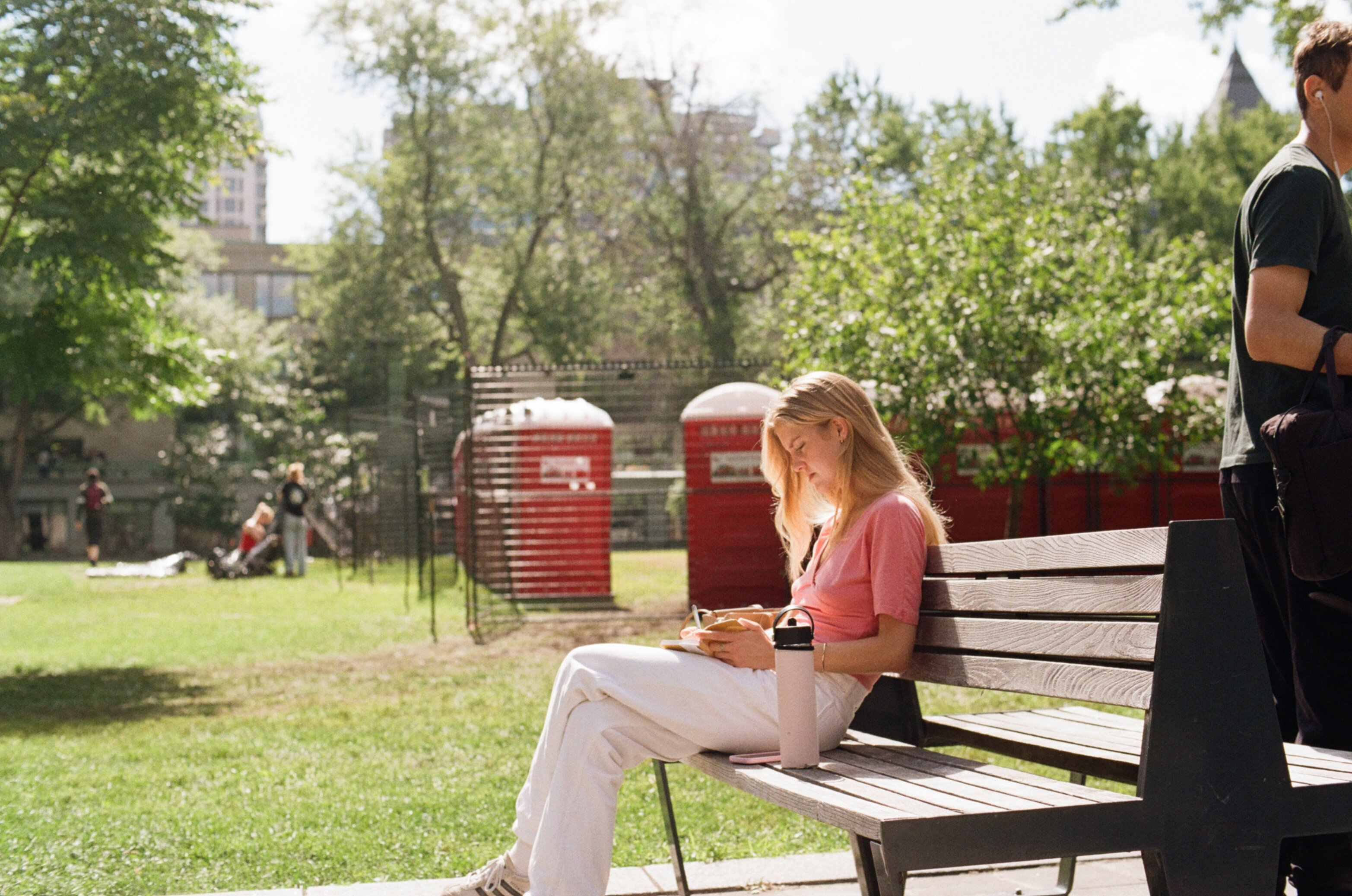 Woman sits on an outdoor bench in the sun with her blond hair backlit